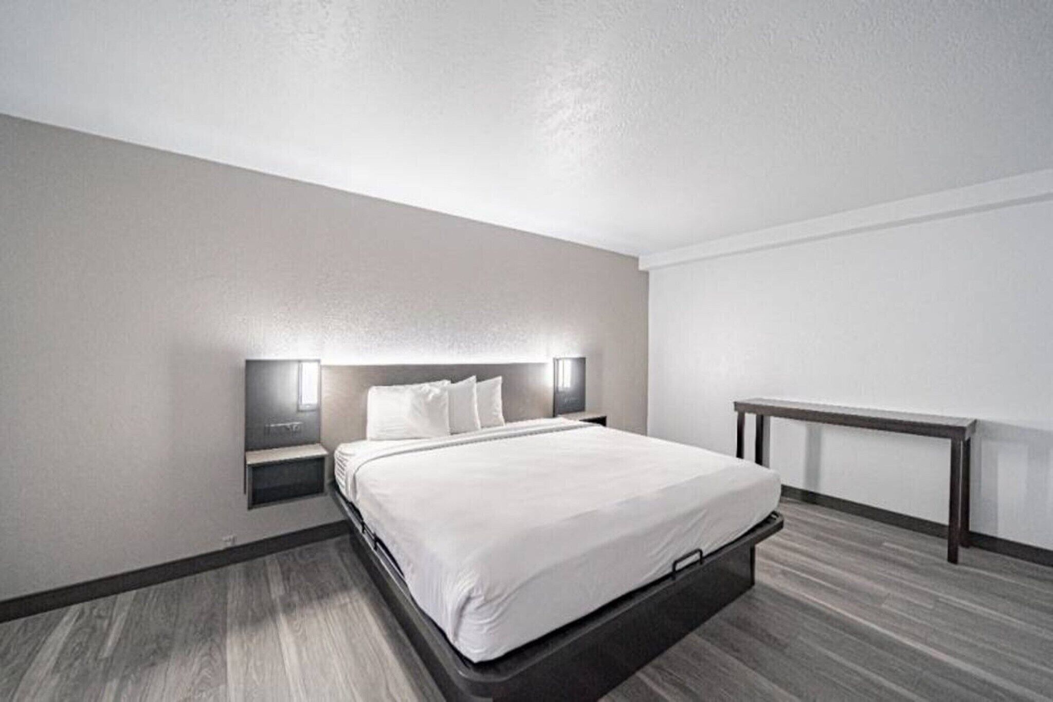 Une chambre d’hôtel moderne équipée d’un lit, de tables de chevet, d’un banc et d’un luminaire fixé au mur.