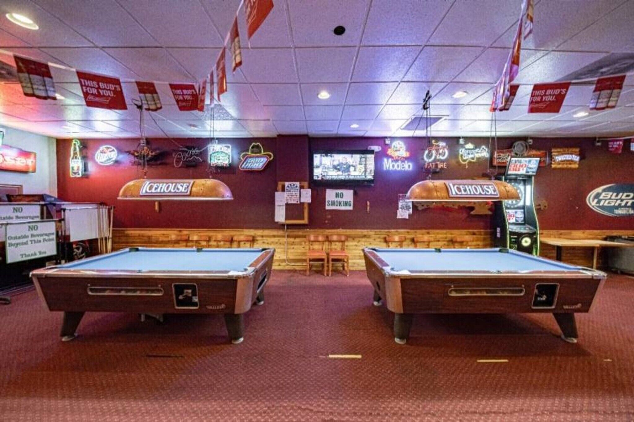 A pool table area with two tables, neon signs, and a television screen.