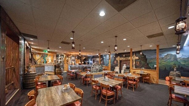 Un restaurant avec des tables et des chaises en bois, un coin bar et des peintures murales.