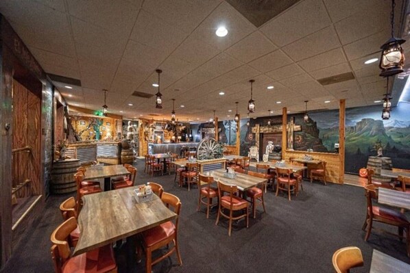A restaurant with wooden tables and chairs, a bar area, and murals on the walls.