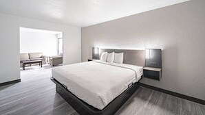 A modern hotel room with a large bed, bedside tables, a sofa, and a window.