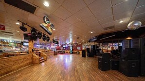 A spacious indoor area with wooden flooring, a stage with speakers, and a counter with various items.