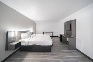 A modern hotel room with a bed, bedside tables, a TV, and a desk.