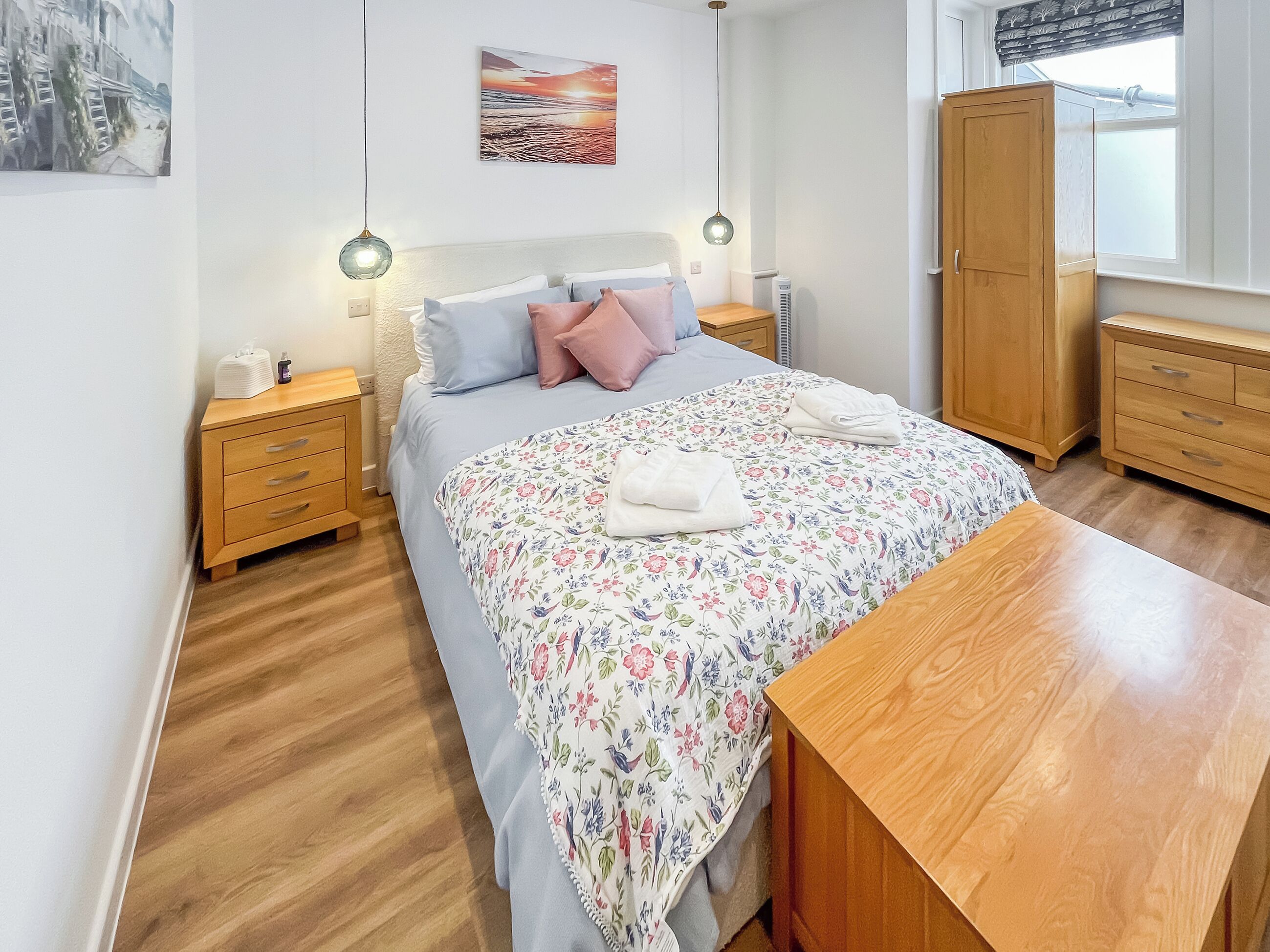 Un dormitorio con cama, mesitas de noche de madera, armario de madera y ventana con vistas.