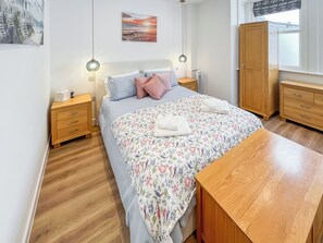A bedroom with a bed, wooden nightstands, a wooden wardrobe, and a window with a view. - Vikings Shore - UK50995 (Broadstairs)