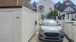 Ein schmaler Weg führt zu einem geparkten Auto in einer Wohngegend mit Häusern an beiden Seiten.