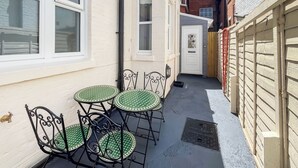 Ein schmaler Gang mit einem weißen Gebäude, einer Tür mit Fensterglas und einem kleinen Tisch mit Stühlen.