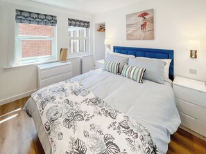 Ein Schlafzimmer mit einem Bett, Nachttischen, einem Fenster mit Jalousien, einem Gemälde an der Wand und einer Ziegelwand.