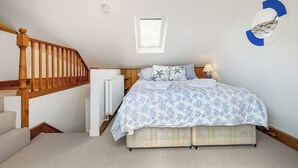 Ein Schlafzimmer mit einem Bett, einem Heizkörper, einem Fenster, einer Holztreppe und einer Wandleuchte.