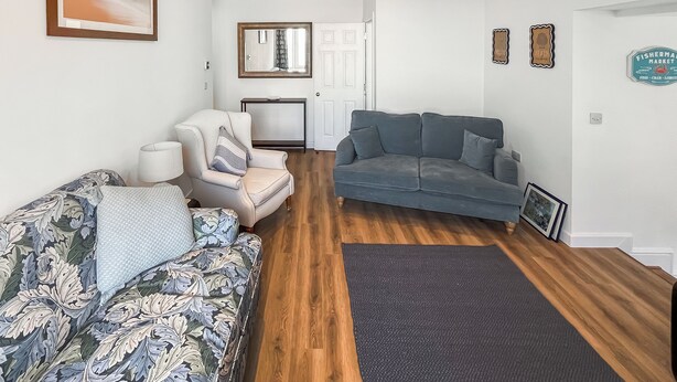 Ein Wohnzimmer mit einer Couch, einem Sessel und einem blauen Sofa. Es gibt einen Holzboden, einen Teppich und ein gerahmtes Bild an der Wand.