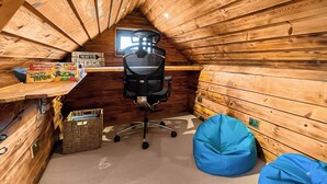 Ein Zimmer mit Holzboden und schrägem Dach, ein schwarzer Bürostuhl, ein Schreibtisch mit Computer, ein Fenster und zwei blaue Sitzsäcke.