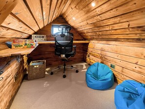 Ein Zimmer mit Holzboden und schrägem Dach, ein schwarzer Bürostuhl, ein Schreibtisch mit Computer, ein Fenster und zwei blaue Sitzsäcke.