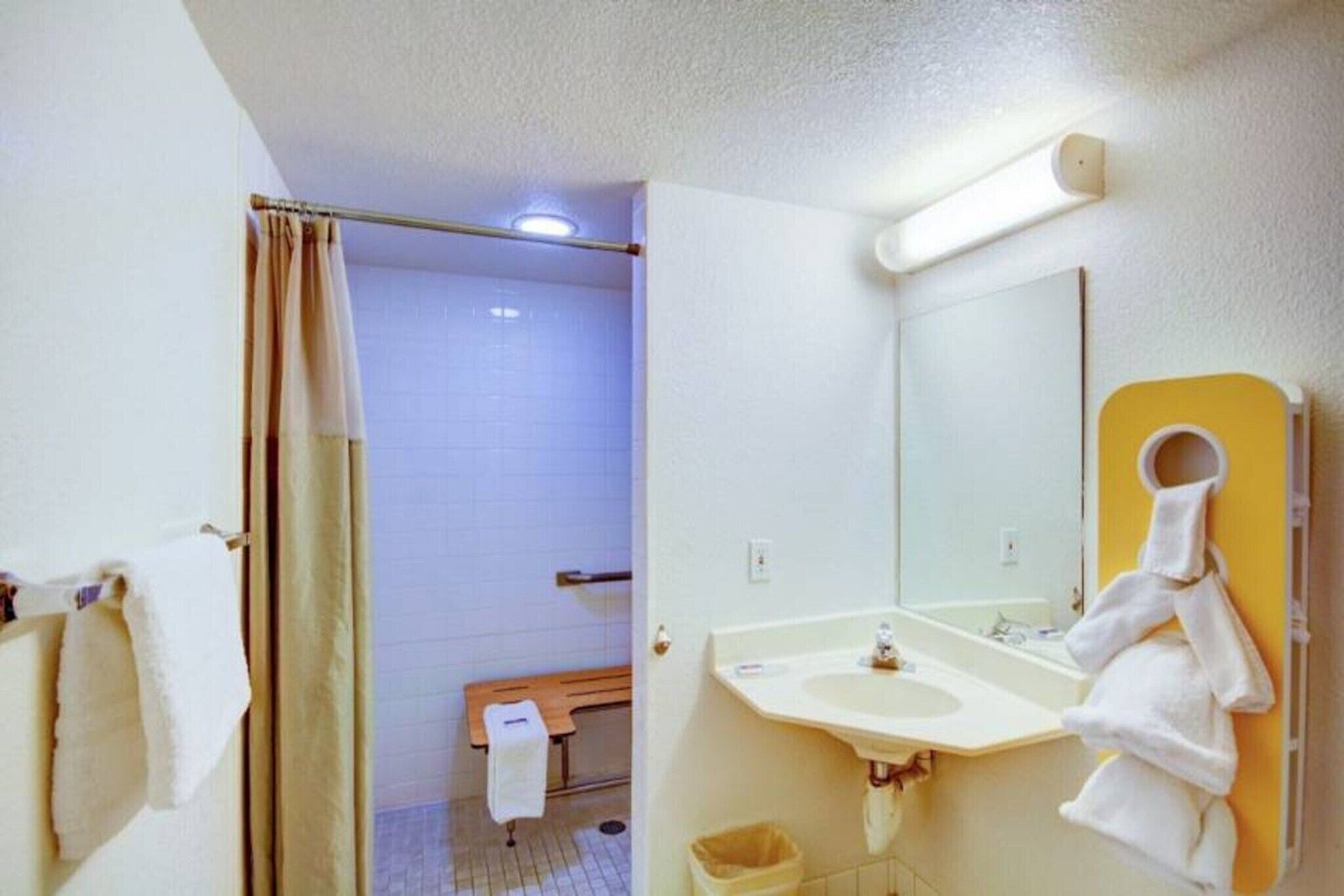 Ein Badezimmer mit Dusche, einer Sitzbank, einem Waschbecken und einem Spiegel.