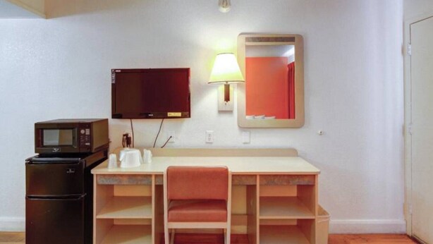 Une pièce compacte comprenant un bureau, une chaise, un four à micro-ondes, un réfrigérateur, une télévision, une lampe et un miroir.
