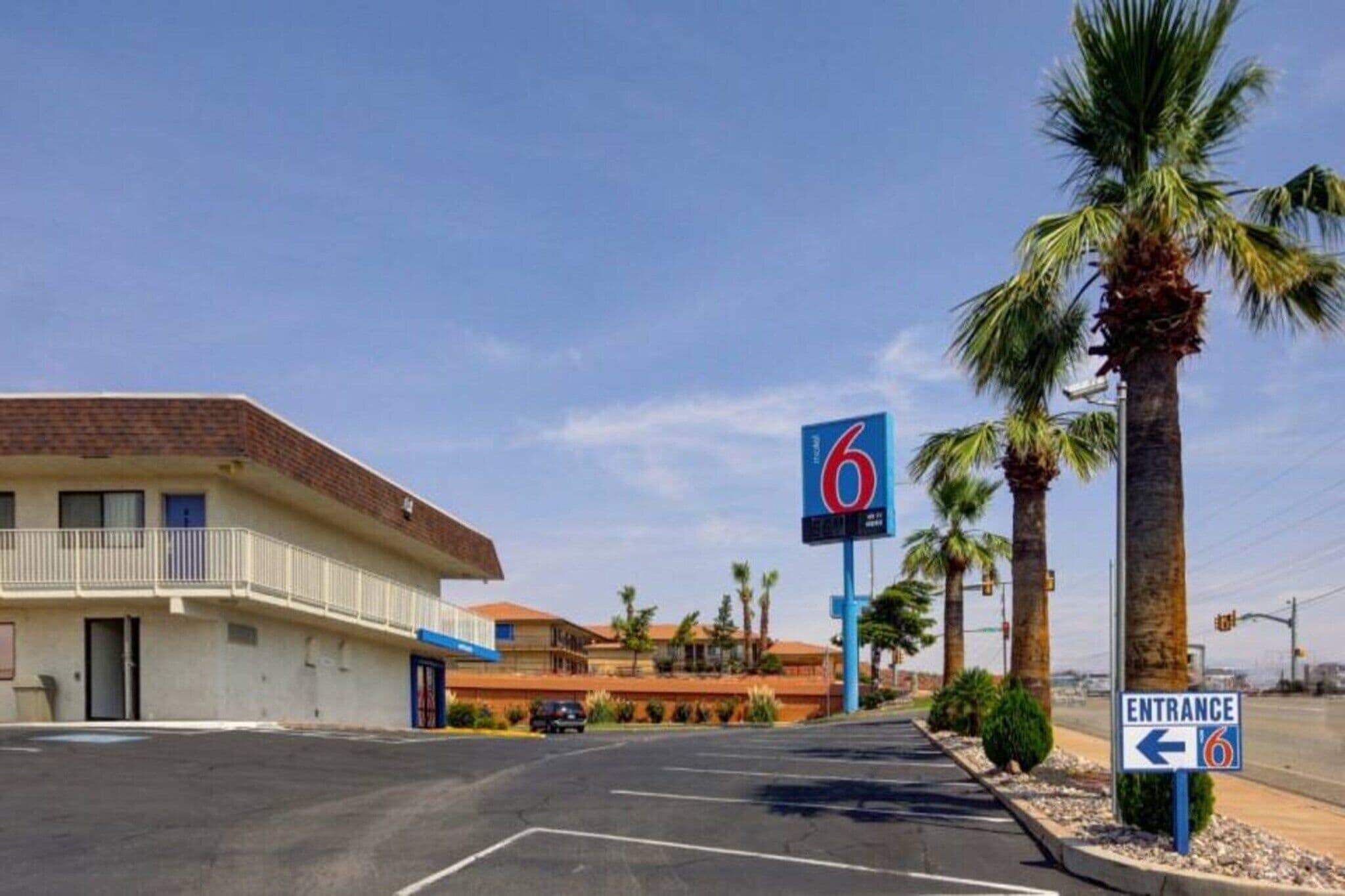 A motel with a sign indicating room number 6, a parking lot, and a clear sky.