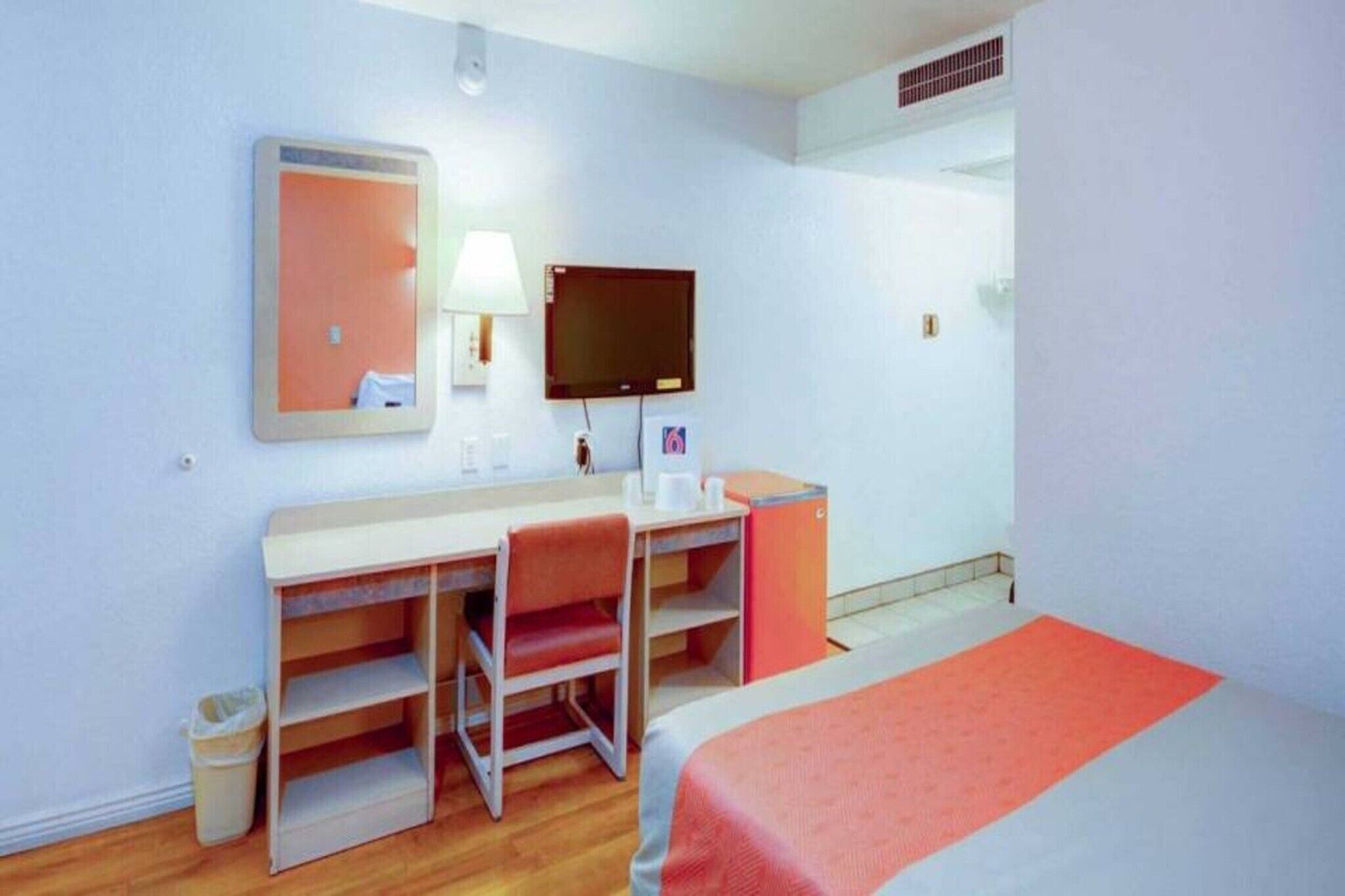 Ein Hotelzimmer mit einem Bett, einem Schreibtisch mit Stuhl, einem Fernseher, einem Spiegel und einem Mülleimer.