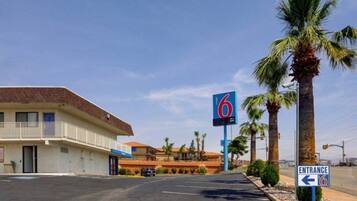 A motel with a sign indicating room number 6, a parking lot, and a clear sky.