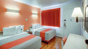 A hotel room with two beds, a table, a chair, a lamp, and a window with curtains. - ADA|2 Beds|RI Shower|Nsmk (St George UT)