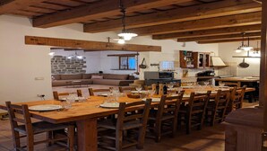 Un comedor con mesas y sillas de madera, una cocina al fondo y una pared de piedra.
