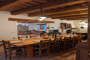 Ein Essbereich mit Holztischen und -stühlen, im Hintergrund eine Küche und eine Steinwand.