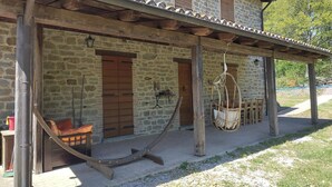 Un edificio de piedra con un porche de madera, una hamaca y una cama.