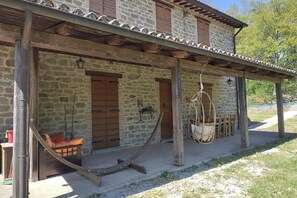 Ein Steinhaus mit einer Holzveranda, einer Hängematte und einem Bett.