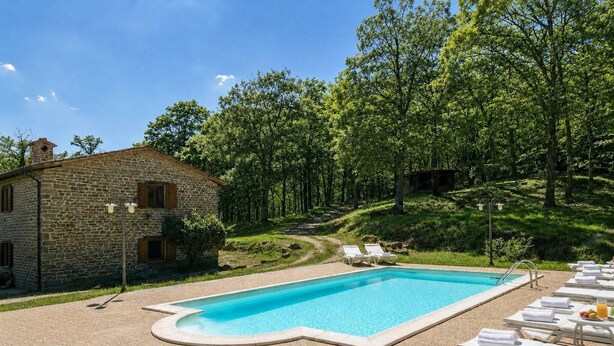 Un edificio de piedra con piscina y sillones de descanso.