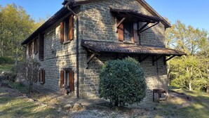 Una casa de piedra con techo inclinado, contraventanas de madera y un pequeño jardín.