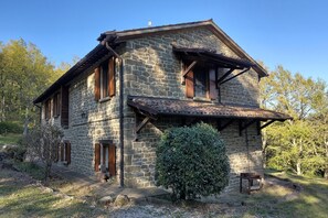 Ein Haus aus Stein mit geneigtem Dach, hölzernen Fensterläden und einem kleinen Garten.