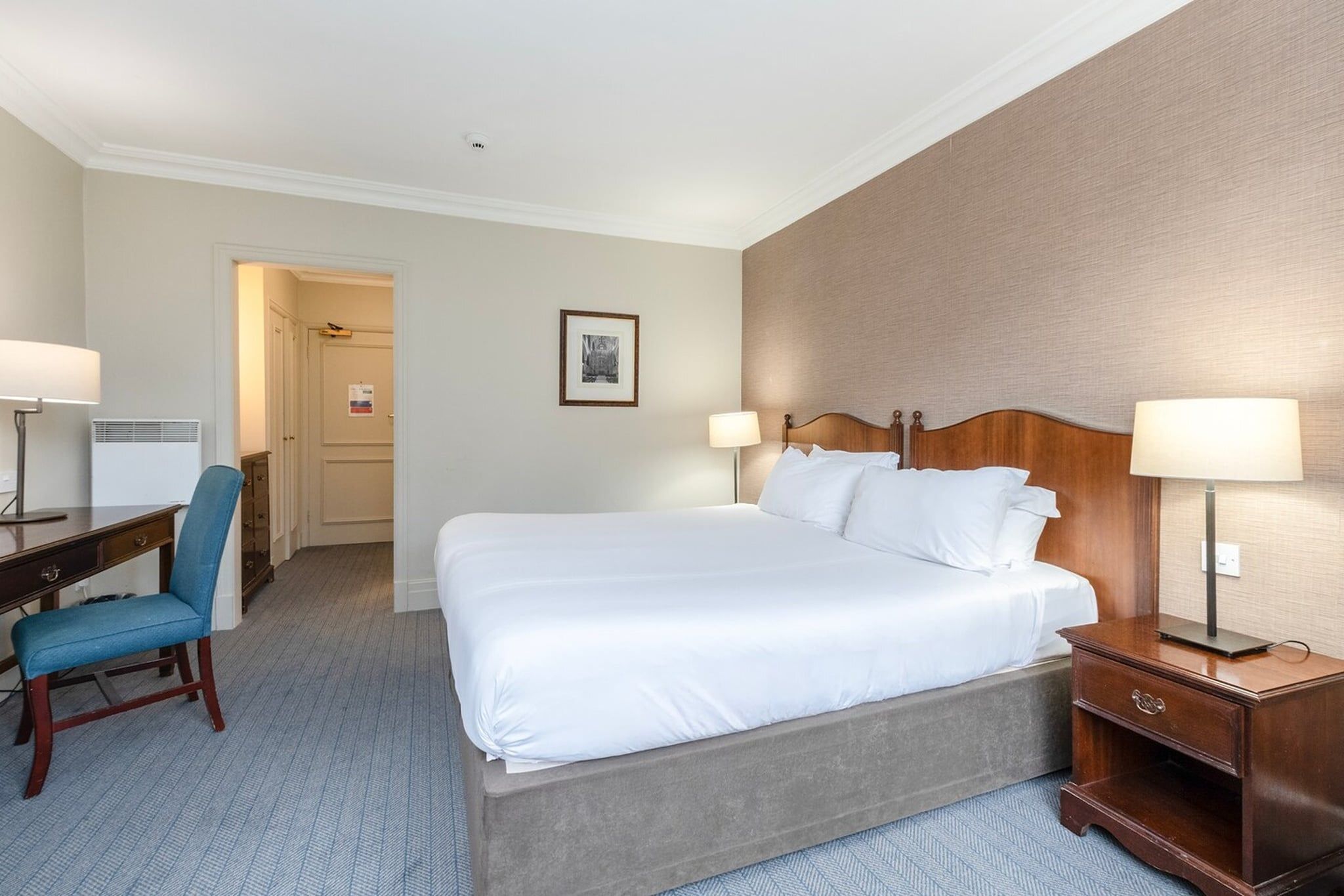 A hotel room with a bed, desk, chair, and two bedside lamps.