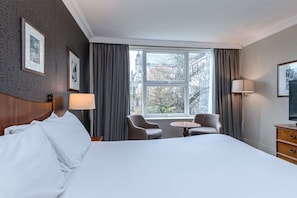 A hotel room with a bed, two armchairs, a small table, a TV, and a window with curtains. - Winchester Wessex Hotel by Sunday Double Room (Winchester)