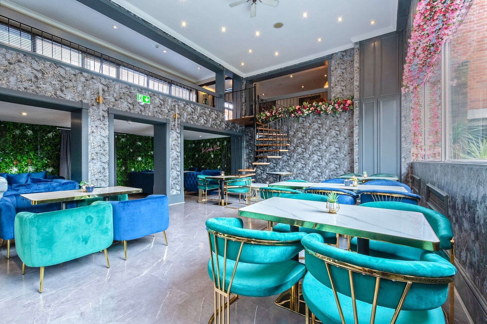 A modern interior with teal upholstered seating, marble flooring, and a staircase leading to an upper level.