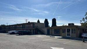 A parking lot with a row of buildings, including a motel with a staircase leading to the entrance. - 1 King Bed|Non-Smoking, Micfridge (Selma)