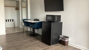 A compact kitchenette with a microwave, a small refrigerator, a table with two chairs, and a TV mounted on the wall. - 1 King Bed|Non-Smoking, Micfridge (Selma)