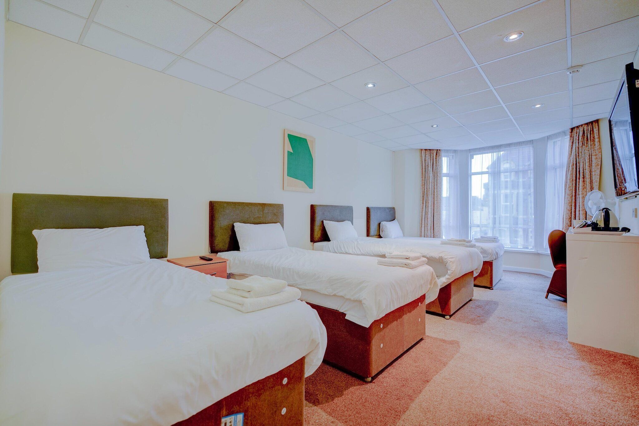 A hotel room with three beds, a desk, and a window with curtains.