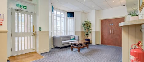 A hotel lobby with a fire exit sign, a reception desk, a sofa, a coffee table, a potted plant, and a fire extinguisher.