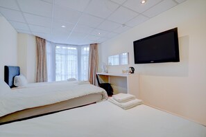 A hotel room with a large bed, a desk with a chair, a flat-screen TV mounted on the wall, and a window with curtains. - OYO Flagship Cardiff Central - Deluxe Quad Room (Cardiff)