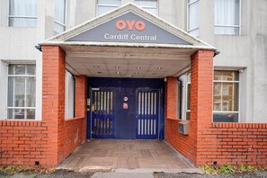 Ein Geb äudeeingang mit einer blauen Tür, einem Schild mit der Aufschrift 'OYO Cardiff Central' und einer Ziegelwand.