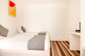 A hotel room with two beds, a television, a desk, and a striped carpet.