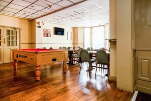 Een pooltafel in een ruimte met houten vloer, stoelen rond een tafel en een deur met glaspanelen.