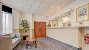 A hotel lobby with a reception desk, a sofa, a coffee table, a potted plant, and a fire extinguisher. - Standard Single Room (Cardiff)