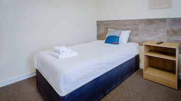 Una cama individual con ropa blanca, un cabecero azul y una mesita de noche de madera con un control remoto.