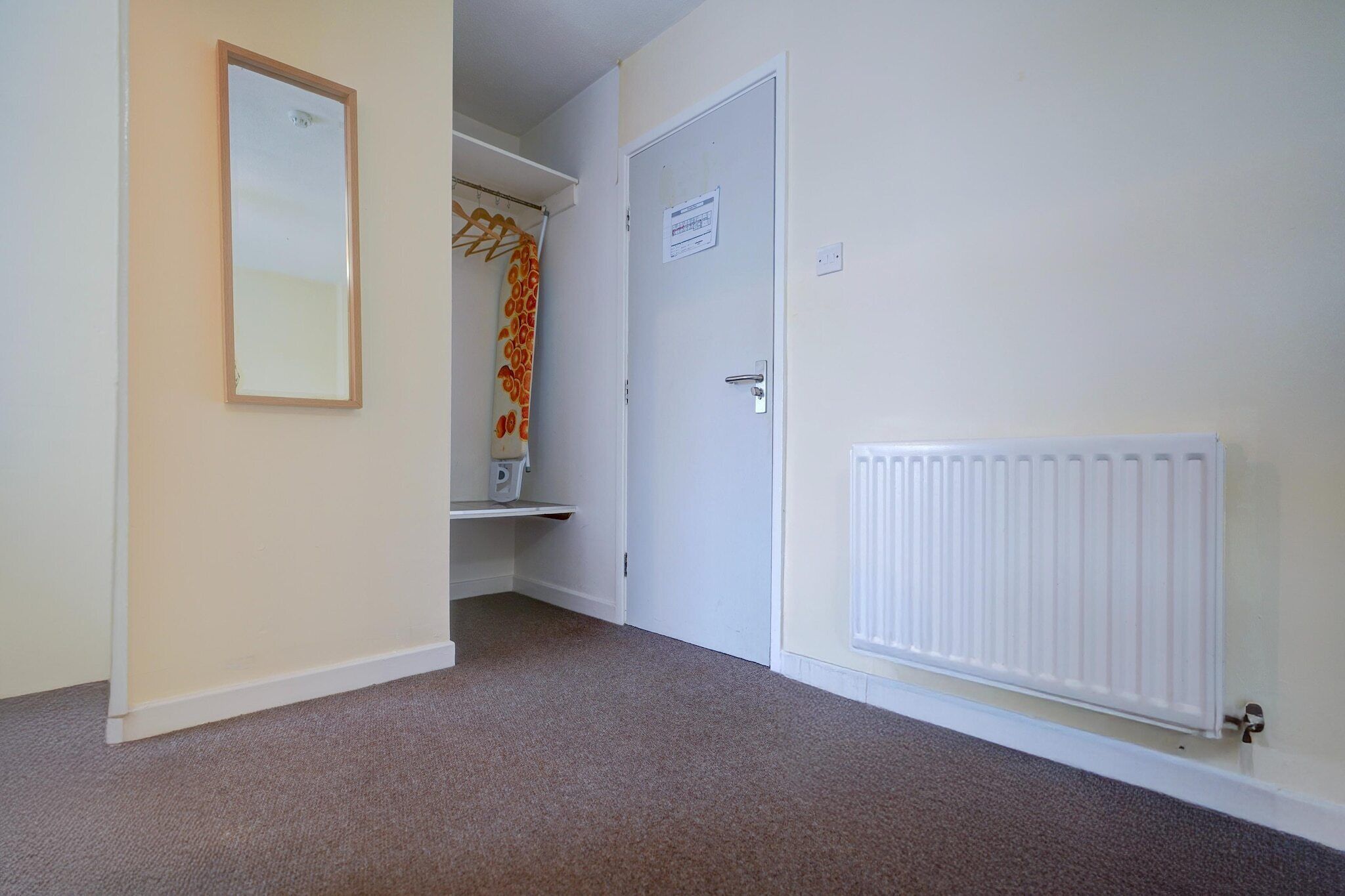 A hallway with a radiator, a door with a sign, and a coat rack with a patterned item.