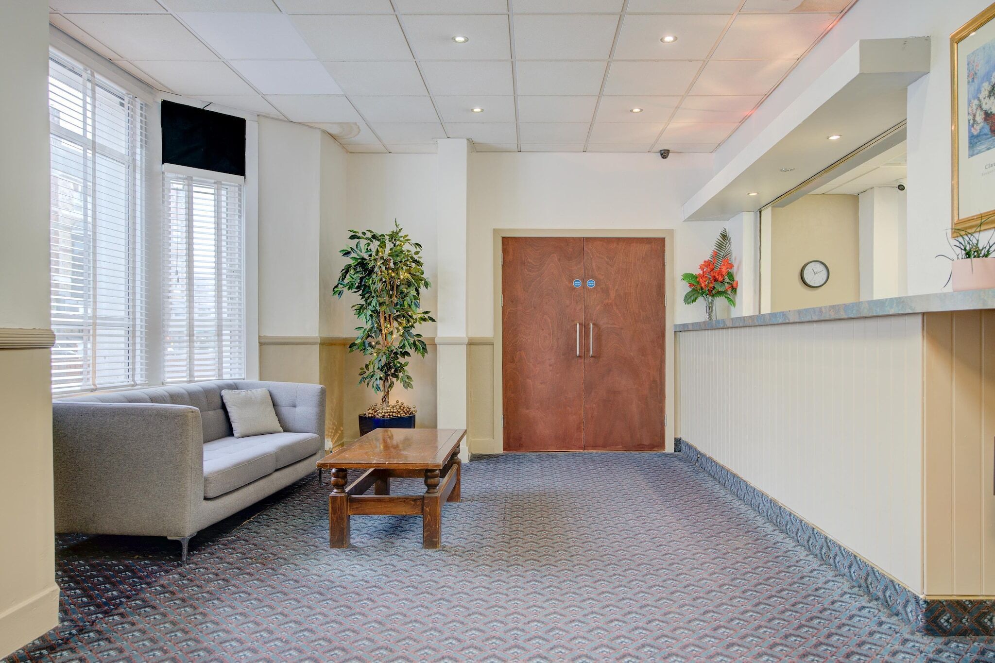 A hotel lobby with a sofa, a wooden table, a potted plant, and a double door.