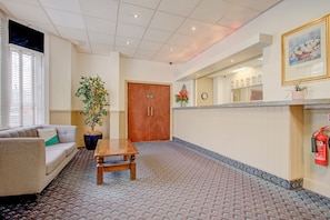 A hotel lobby with a reception desk, a wooden door, a sofa, a coffee table, and a potted plant. - OYO Flagship Cardiff Central - Deluxe Double Room (Cardiff)