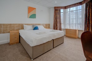 A double bed with a beige headboard, two bedside tables, a small wooden dresser, and a large window with curtains. - OYO Flagship Cardiff Central - Deluxe Double Room (Cardiff)