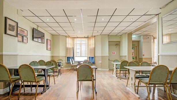 A conference room with multiple tables and chairs, a tiled ceiling, and framed artwork on the walls. - Superior Triple Room (Cardiff)