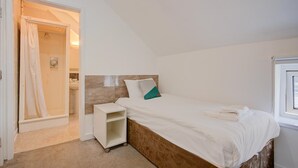 Un dormitorio con una cama individual, una mesita de noche, un pequeño estante y un rincón de ducha.