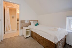 Un dormitorio con una cama individual, una mesita de noche, un pequeño estante y un rincón de ducha.