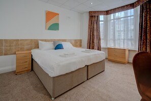 A double bed with a beige headboard, two bedside tables, a small wooden dresser, and a large window with curtains. - OYO Flagship Cardiff Central - Deluxe Twin Room (Cardiff)